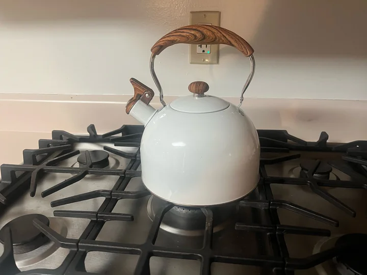 White LONFFERY stovetop tea kettle with wood-grain handle accents sitting on a gas stove