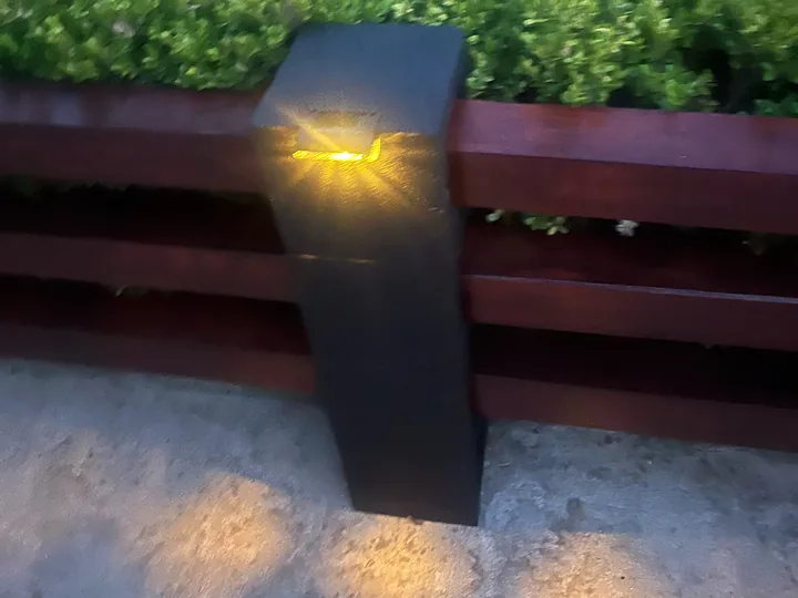 Warm Mancra solar fence light glowing on a dark wooden post at dusk