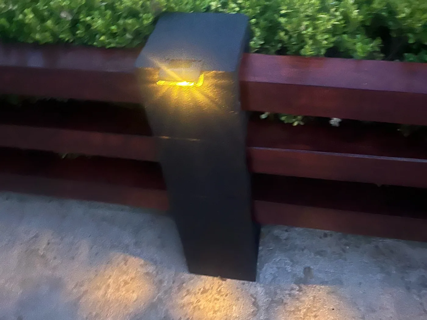 Warm Mancra solar fence light glowing on a dark wooden post at dusk
